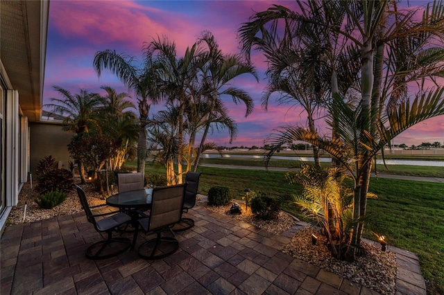 patio terrace at dusk featuring a water view and a lawn