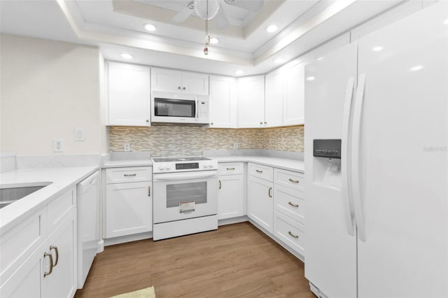 kitchen with decorative backsplash, a raised ceiling, white cabinetry, light hardwood / wood-style floors, and white appliances