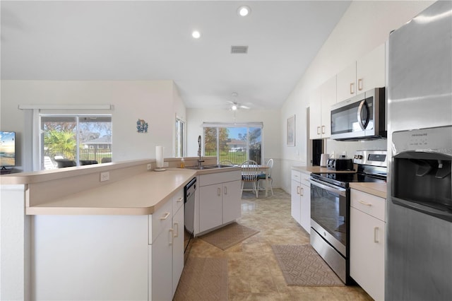 kitchen with appliances with stainless steel finishes, white cabinetry, a wealth of natural light, and vaulted ceiling