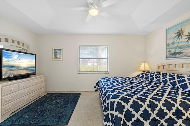 bedroom with a raised ceiling, light carpet, and ceiling fan