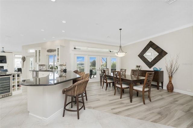 dining space featuring french doors, beverage cooler, sink, ornamental molding, and light hardwood / wood-style flooring