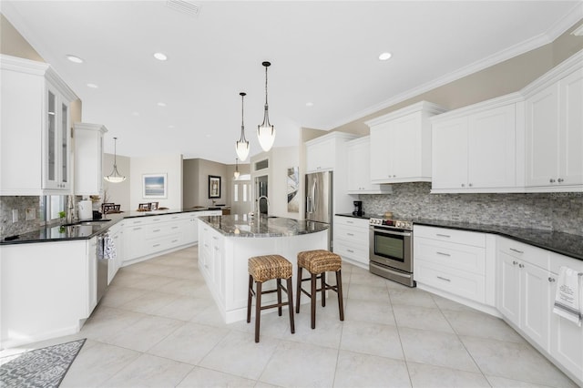 kitchen featuring stainless steel appliances, a center island with sink, ornamental molding, hanging light fixtures, and white cabinets