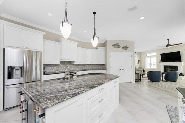 kitchen with ornamental molding, a center island with sink, stainless steel fridge, white cabinetry, and pendant lighting