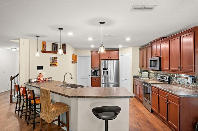 kitchen featuring stainless steel appliances, decorative light fixtures, sink, a breakfast bar, and light hardwood / wood-style floors