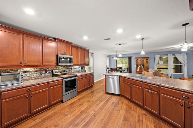 kitchen featuring tasteful backsplash, appliances with stainless steel finishes, pendant lighting, sink, and light hardwood / wood-style flooring