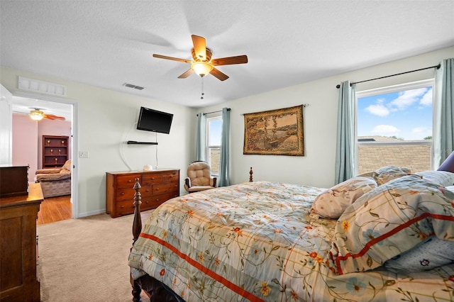 bedroom with multiple windows, a textured ceiling, light colored carpet, and ceiling fan