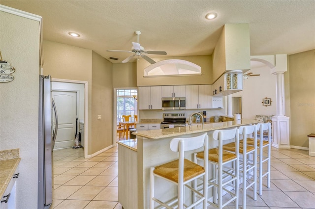 kitchen with white cabinetry, light stone countertops, decorative columns, a breakfast bar, and appliances with stainless steel finishes