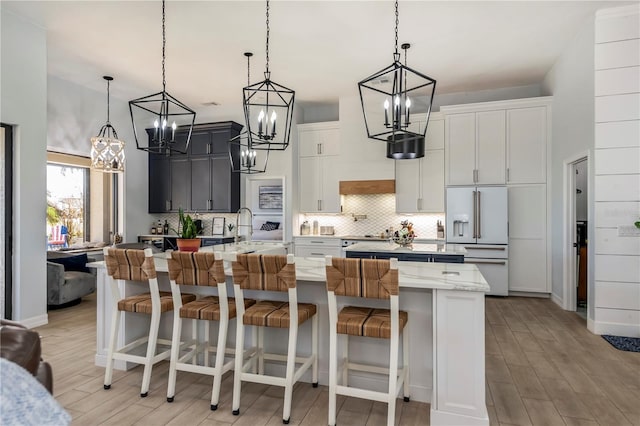 kitchen featuring a large island with sink, high end white fridge, pendant lighting, and a kitchen breakfast bar