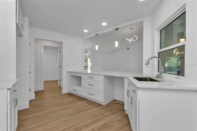 kitchen featuring decorative light fixtures, sink, white cabinets, kitchen peninsula, and light hardwood / wood-style flooring