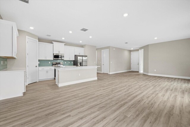 kitchen featuring white cabinets, decorative backsplash, an island with sink, light hardwood / wood-style floors, and stainless steel appliances