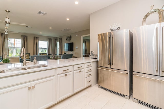 kitchen with white cabinetry, sink, light stone counters, and stainless steel fridge