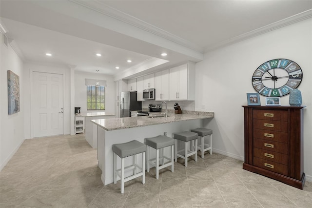 kitchen with kitchen peninsula, appliances with stainless steel finishes, light stone countertops, ornamental molding, and white cabinets