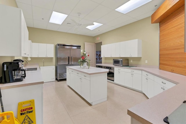 kitchen featuring stainless steel appliances, white cabinetry, a kitchen island, and a drop ceiling