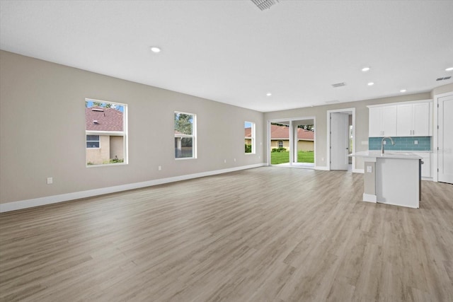 unfurnished living room featuring sink and light hardwood / wood-style floors