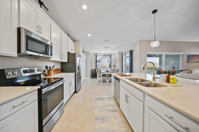 kitchen with white cabinets, light tile patterned floors, appliances with stainless steel finishes, sink, and decorative light fixtures