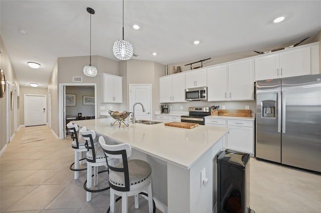 kitchen with an island with sink, appliances with stainless steel finishes, white cabinetry, sink, and decorative light fixtures