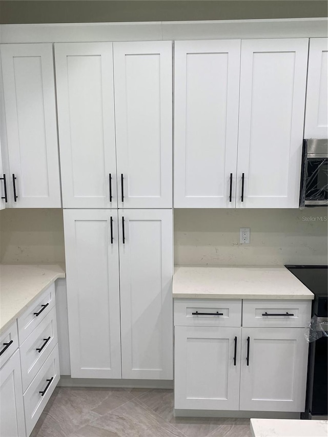 kitchen featuring white cabinetry, light stone countertops, and range