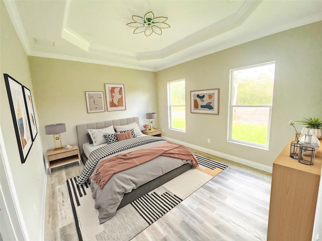 bedroom with light wood-type flooring, a tray ceiling, and crown molding