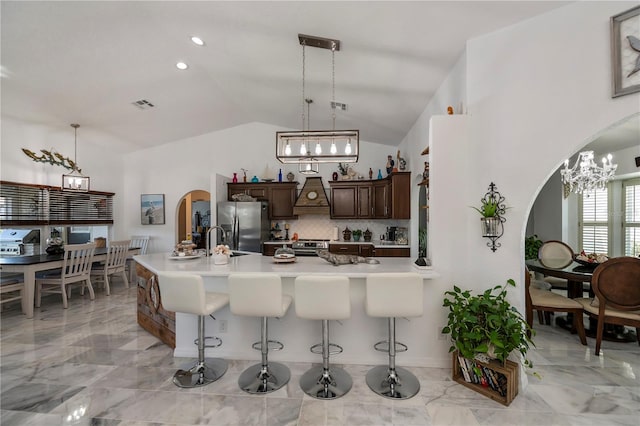 kitchen featuring stainless steel appliances, vaulted ceiling, kitchen peninsula, dark brown cabinetry, and a kitchen breakfast bar