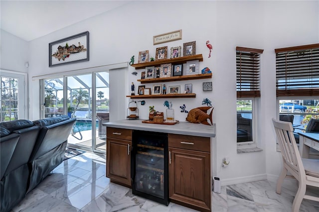 bar with wine cooler, dark brown cabinets, a healthy amount of sunlight, and a towering ceiling