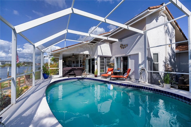 view of swimming pool featuring a patio, ceiling fan, glass enclosure, and a water view