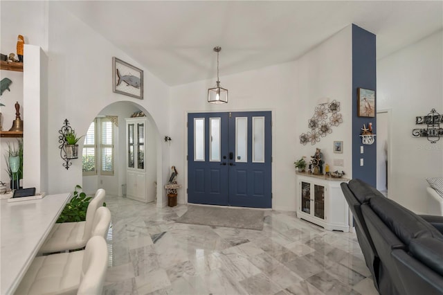 foyer entrance featuring arched walkways, marble finish floor, and high vaulted ceiling