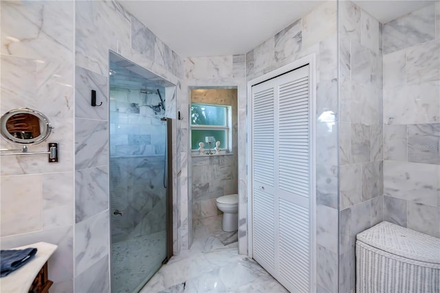 bathroom featuring toilet, marble finish floor, a tile shower, a closet, and tile walls