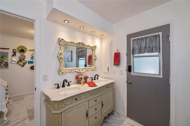 bathroom with a sink, baseboards, marble finish floor, and double vanity