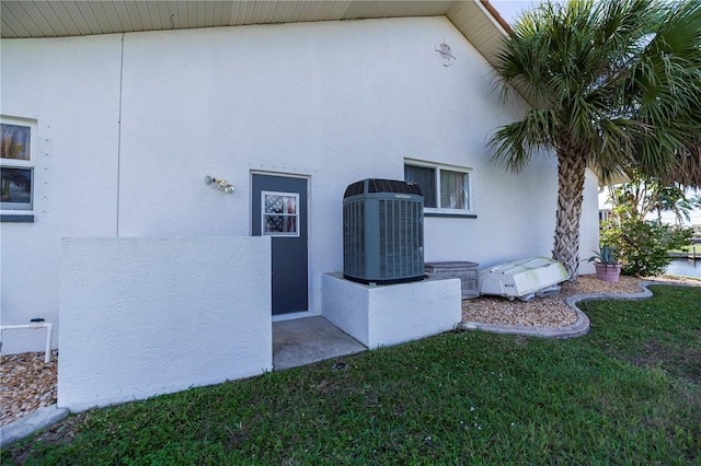 exterior space featuring central air condition unit, stucco siding, and a lawn