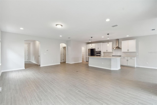 kitchen with white cabinetry, light wood-type flooring, decorative light fixtures, an island with sink, and wall chimney exhaust hood