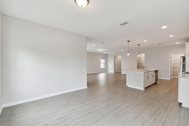 kitchen with a kitchen island with sink, pendant lighting, sink, white cabinets, and light hardwood / wood-style flooring