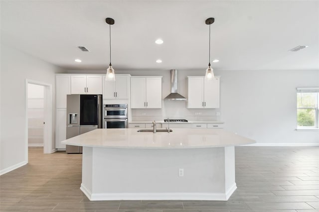 kitchen featuring wall chimney exhaust hood, a center island with sink, sink, and appliances with stainless steel finishes