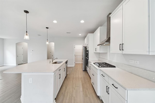 kitchen with stainless steel appliances, light wood-type flooring, decorative light fixtures, white cabinets, and a kitchen island with sink