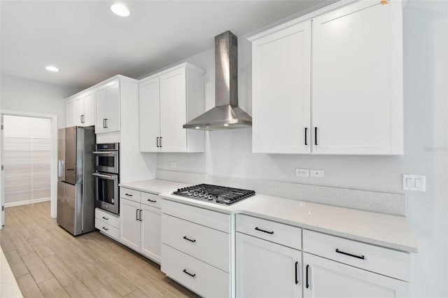 kitchen featuring wall chimney range hood, stainless steel appliances, light hardwood / wood-style floors, and white cabinets