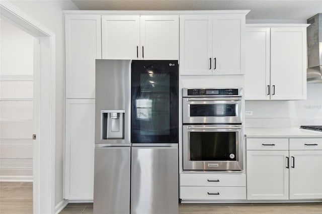 kitchen featuring white cabinets, stainless steel appliances, wall chimney exhaust hood, and light hardwood / wood-style flooring