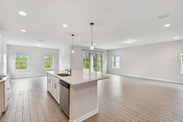 kitchen featuring sink, an island with sink, stainless steel dishwasher, pendant lighting, and light wood-type flooring