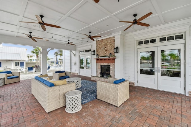 living room with ornate columns, french doors, coffered ceiling, an outdoor stone fireplace, and ceiling fan