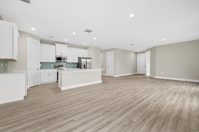 kitchen featuring light wood-type flooring, backsplash, white cabinetry, stainless steel appliances, and a center island with sink