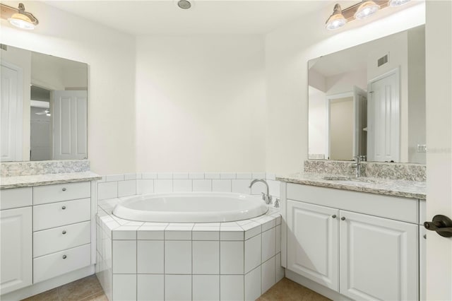 bathroom with tile patterned flooring, vanity, and a relaxing tiled tub