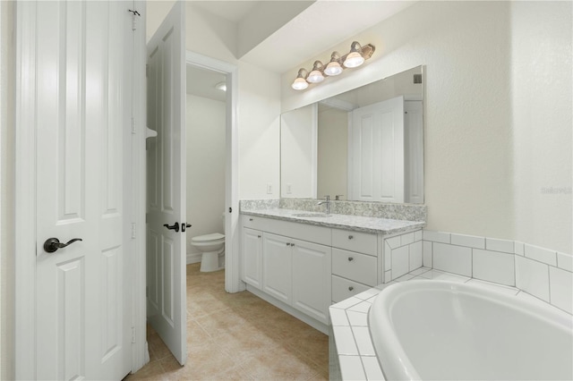 bathroom featuring tiled tub, tile patterned flooring, vanity, and toilet