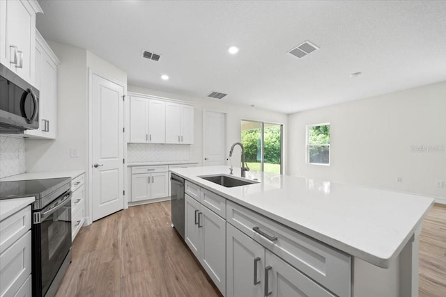 kitchen featuring sink, wood-type flooring, decorative backsplash, a center island with sink, and appliances with stainless steel finishes