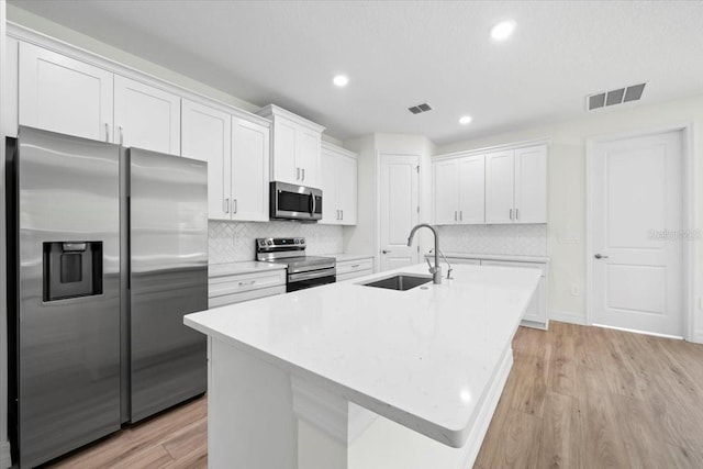 kitchen featuring a kitchen island with sink, white cabinets, stainless steel appliances, and light hardwood / wood-style floors