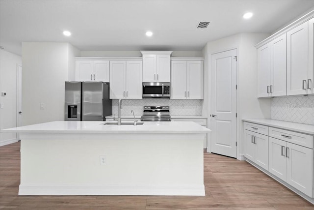 kitchen with white cabinets, appliances with stainless steel finishes, and a center island with sink