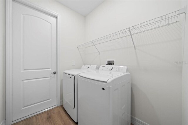 clothes washing area with washer and clothes dryer and hardwood / wood-style flooring