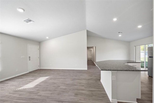 kitchen featuring dark stone countertops, dark hardwood / wood-style flooring, a center island, and vaulted ceiling