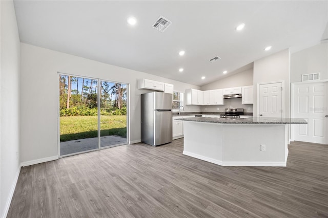 kitchen featuring dark stone counters, stainless steel appliances, white cabinetry, hardwood / wood-style floors, and a kitchen island