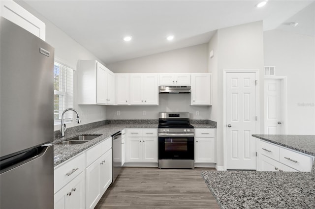 kitchen featuring appliances with stainless steel finishes, vaulted ceiling, sink, stone counters, and white cabinets