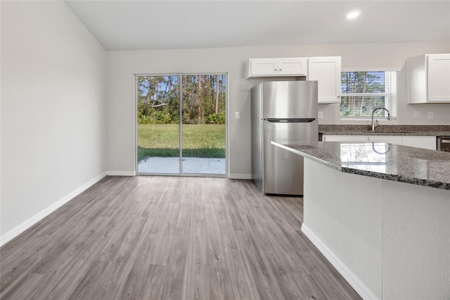 kitchen featuring stainless steel refrigerator, dark stone countertops, white cabinets, and light wood-type flooring