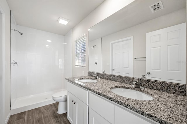 bathroom featuring hardwood / wood-style flooring, vanity, toilet, and tiled shower