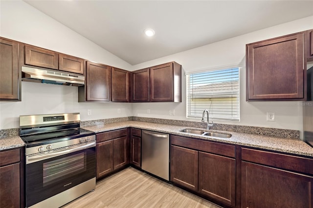 kitchen with light stone countertops, appliances with stainless steel finishes, light wood-type flooring, sink, and lofted ceiling